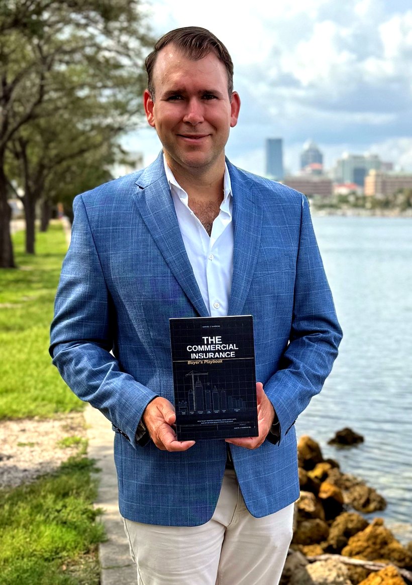 Samuel J. Summers holding his book, The Commercial Insurance Buyer&rsquo;s Playbook, on the Tampa waterfront